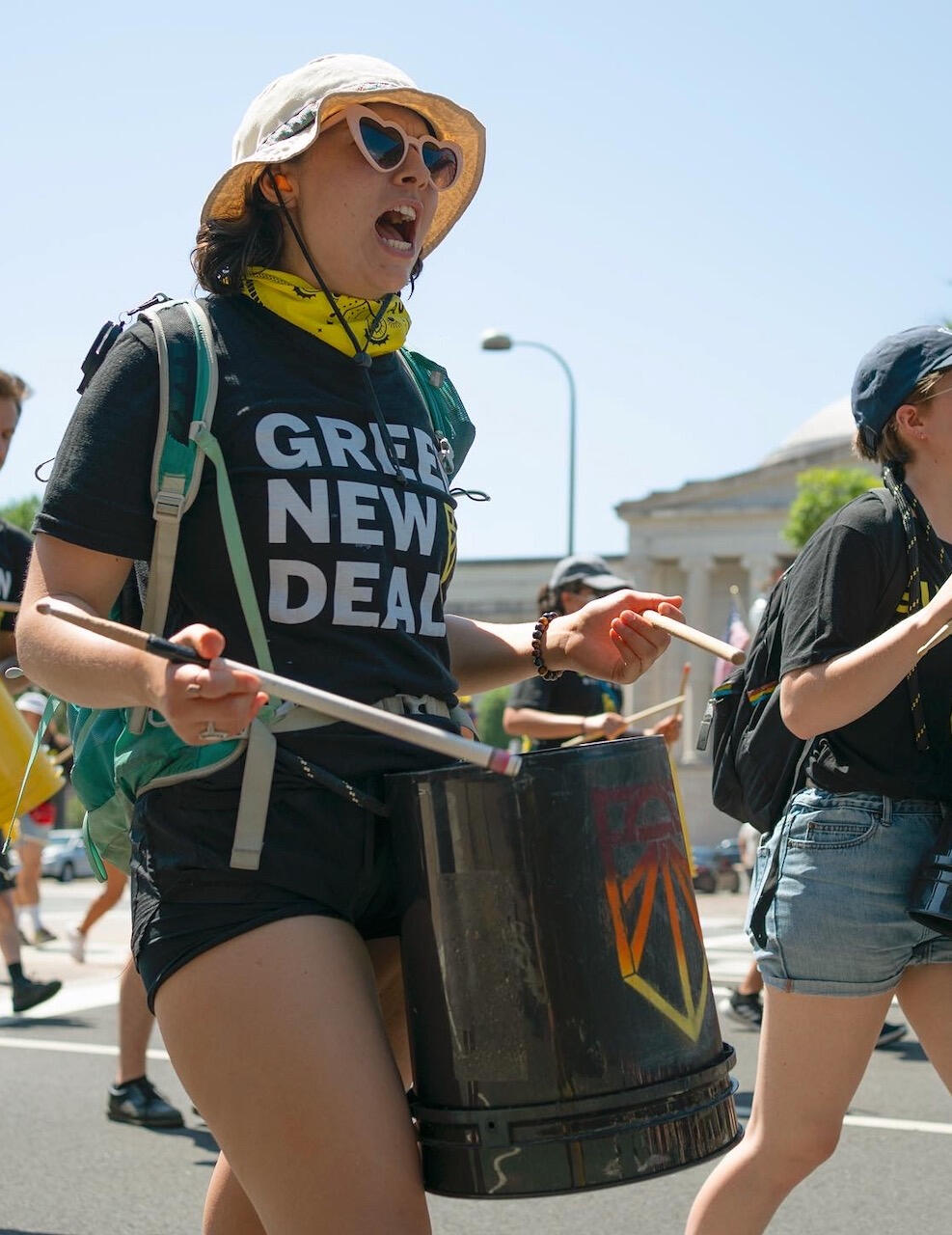 Rachael with bucket drum, "Green New deal" shirt